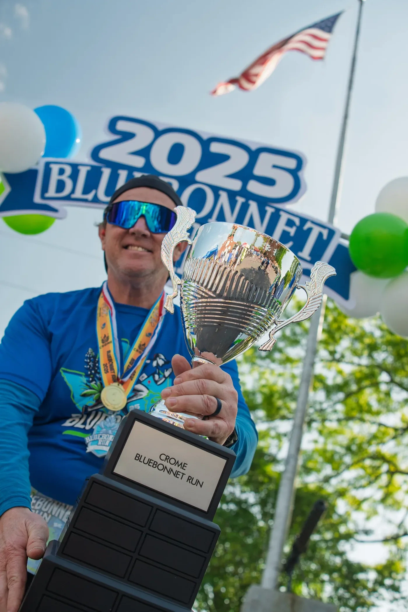 A runner holding a CROME Bluebonnet Run trophy in front of the 2025 event backdrop
