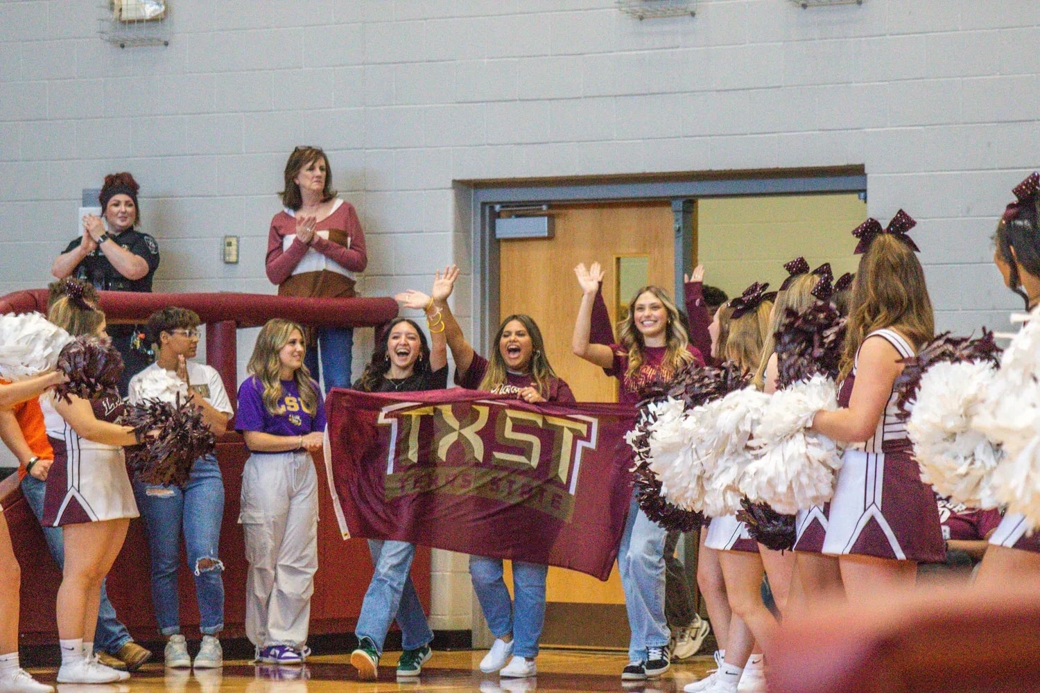 Students and cheerleaders celebrating with a Texas State banner at the 2024 Ennis High School senior pep rally
